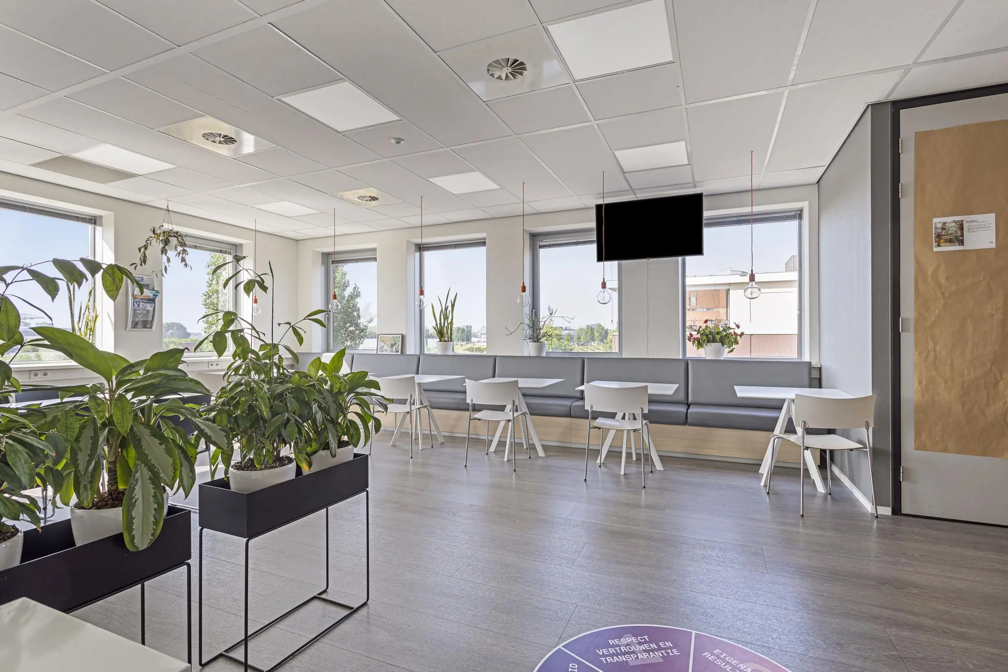 Moderne en lichte kantineruimte aan de Fascinatio Boulevard met grote ramen, planten en zitplaatsen langs de wand.